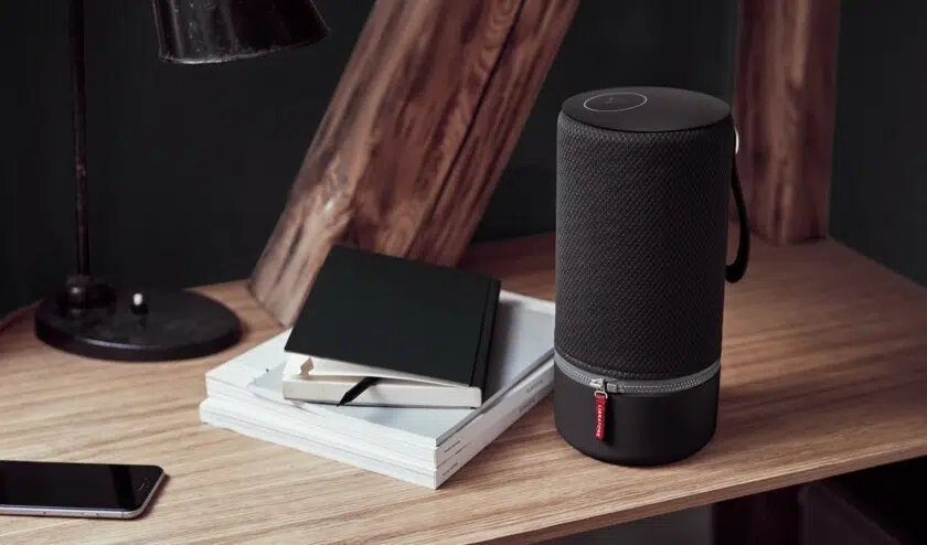 Libratone Zipp Alexa speaker in black on wood table with journals to the left.