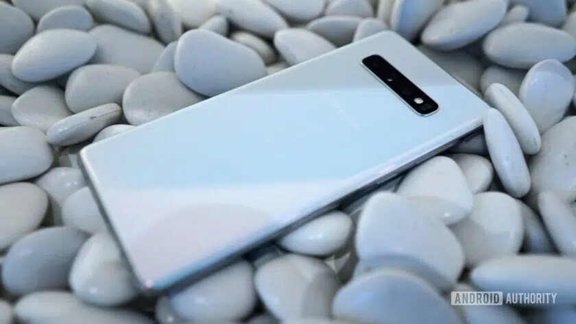 Back side photo of a white Samsung Galaxy S10 Plus placed on rocks.