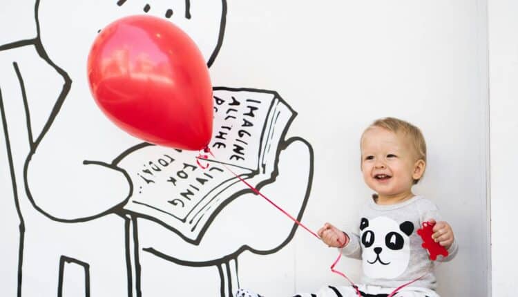 un enfant souriant, un ballon rouge à la main